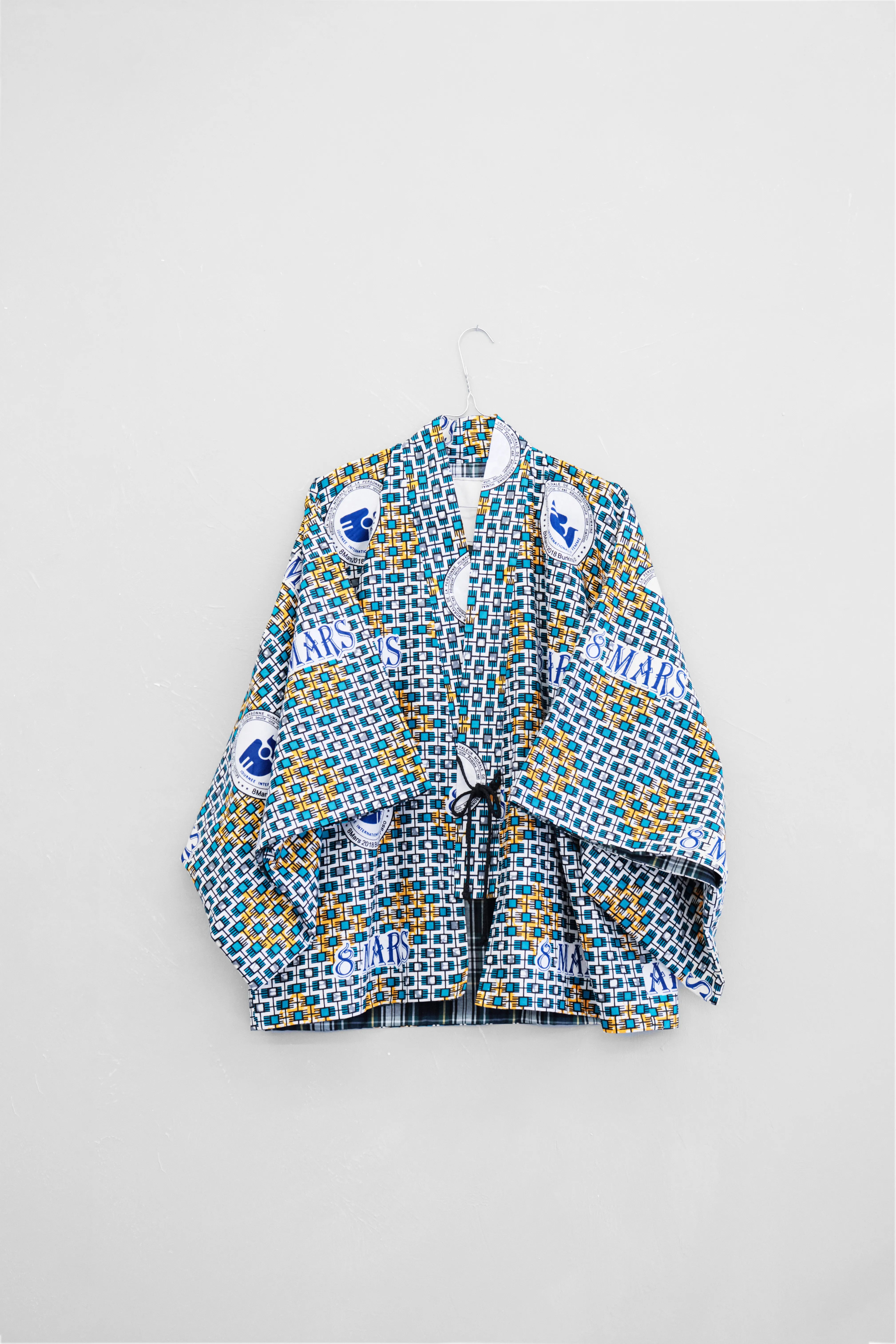 Kmono Bruce 8 mars wax bleu blanc, motif abstrait Journée droits femmes, doublure écossais vert bleu blanc coton, sur cintre vu de face

